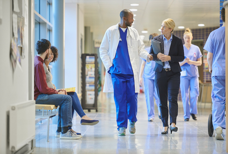 Image of people sitting and HCPs walking in the hallway of  hospital.  